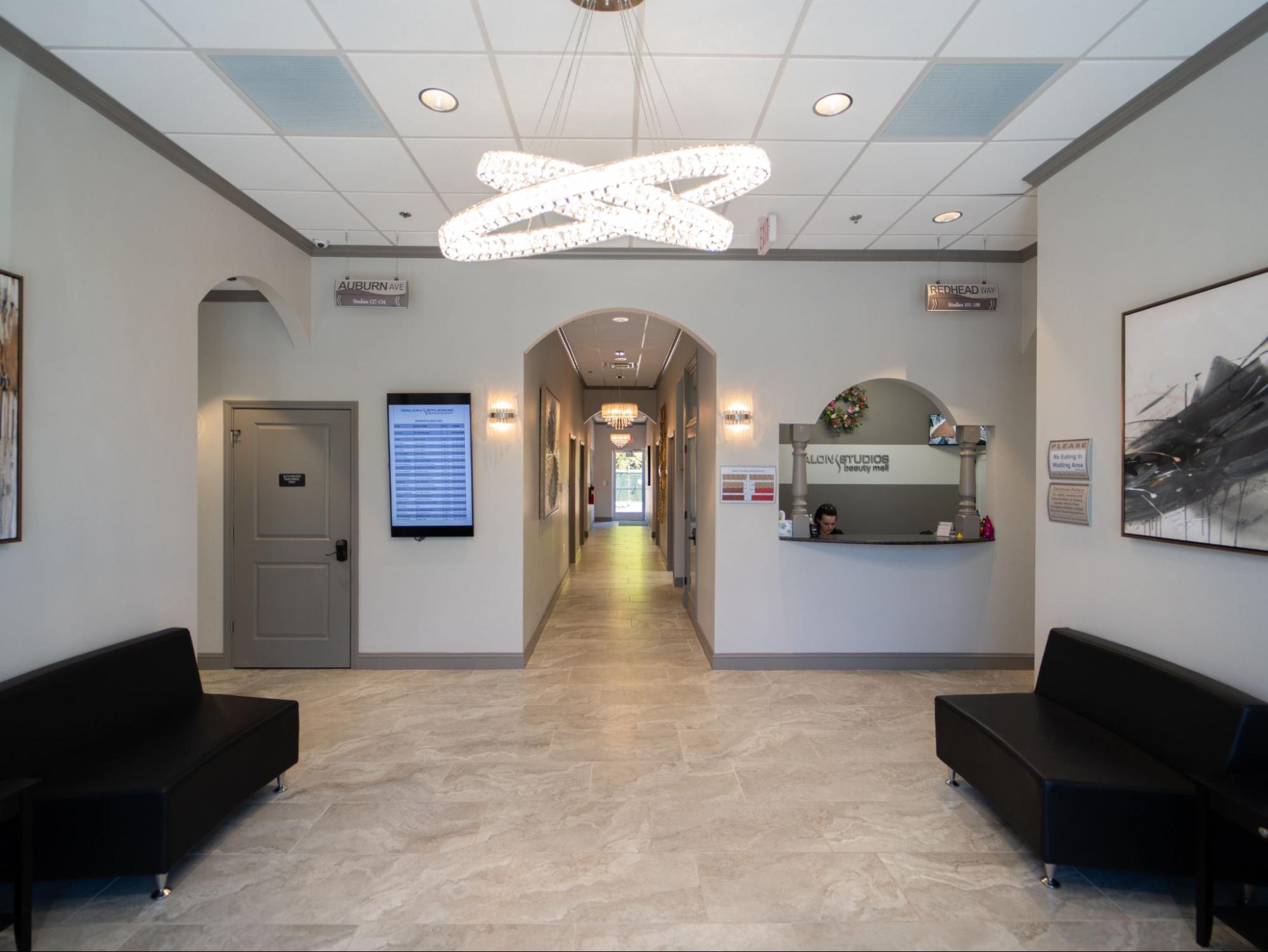 Beauty Salon Studio Franchise - Modern and Welcoming Reception Area Beauty salon studio franchise reception with black benches,
chandelier, hallway, digital display, and front desk.