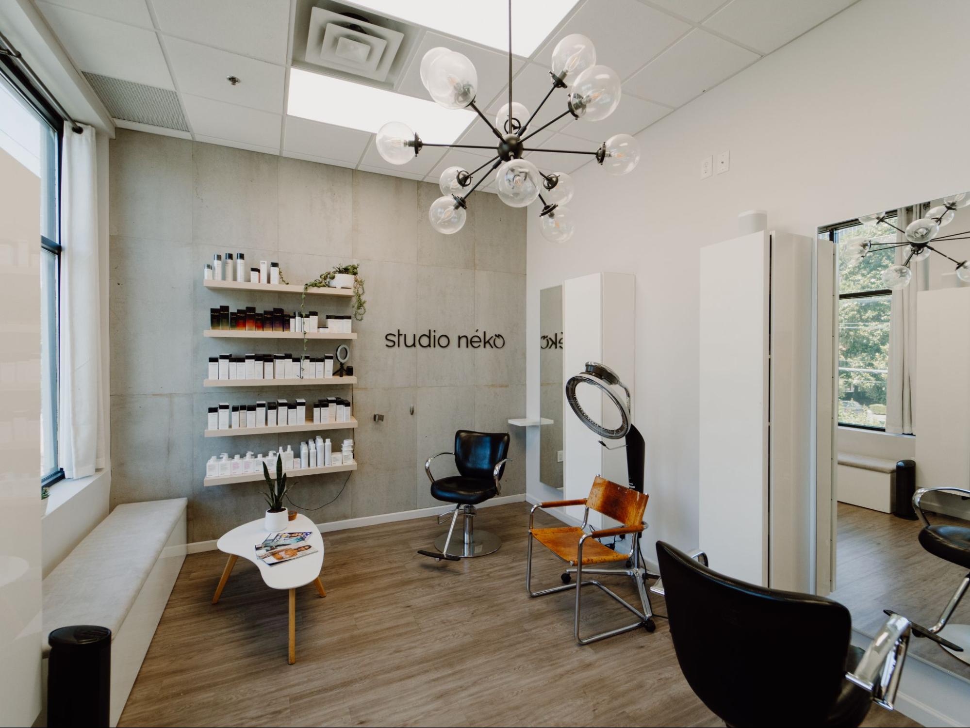 Rent beauty salon studio featuring styling stations, product display
  shelves, modern chandelier, and bright windows.